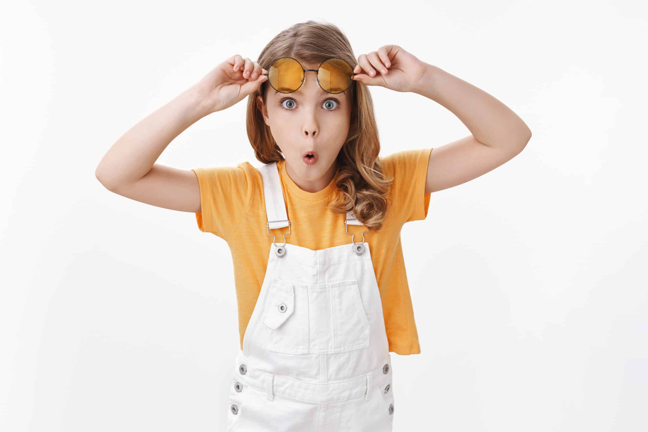 Surprised curious gorgeous tender littlr girl, blond haircut and blue eyes, taking-off sunglasses amazed, stare camera wondered, fold lips astonished and impressed, stand white background.